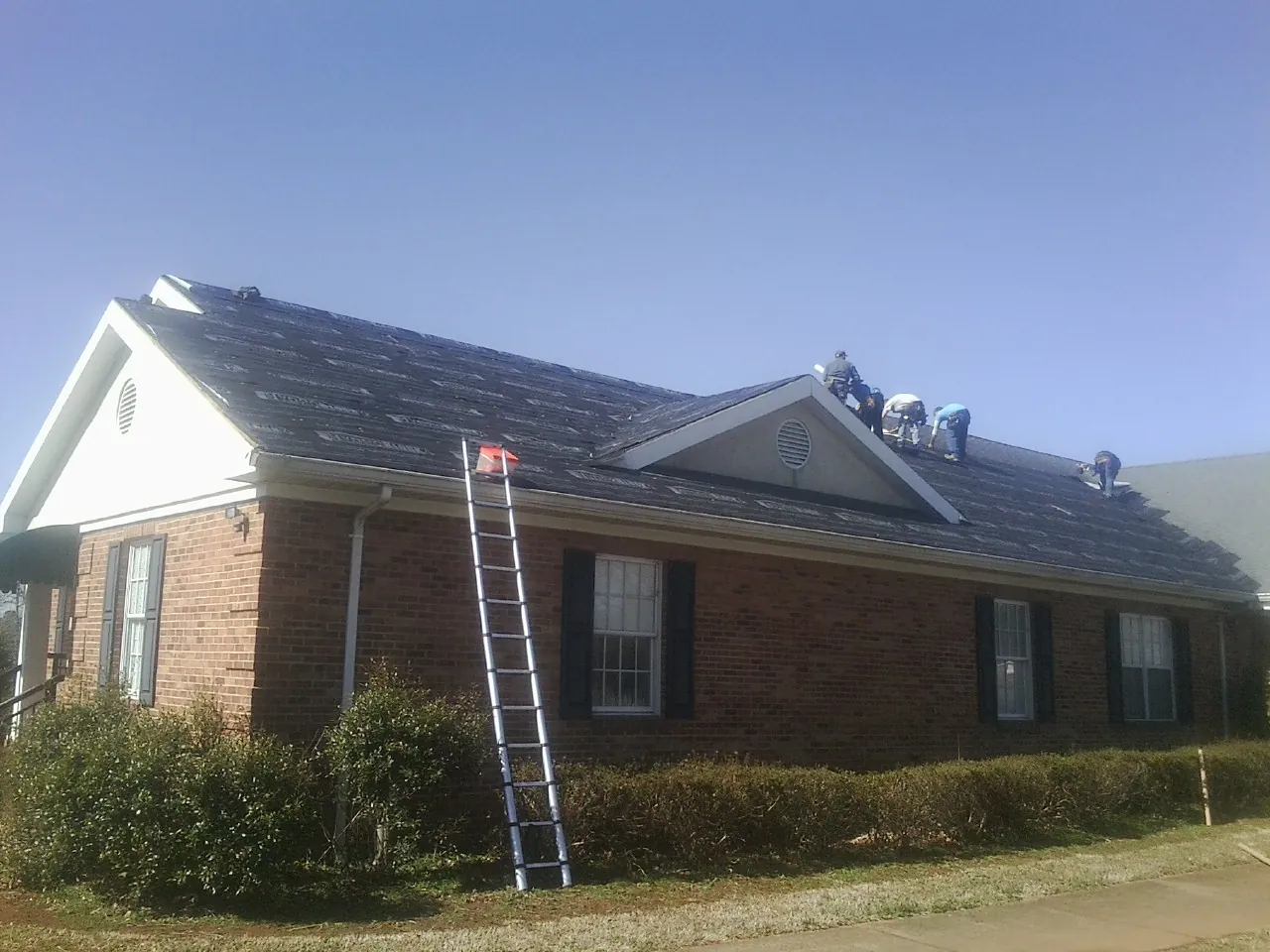 Crew tearing shingles off a brick ranch roof with a ladder set — Metal Roof Repair work by our crew in Talisheek