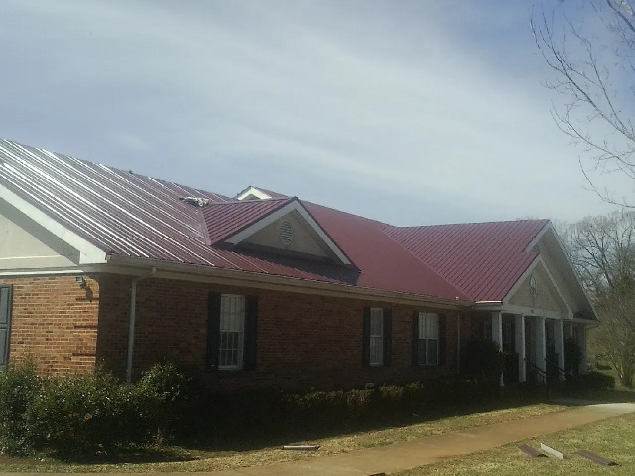 Red metal roof with gabled entries on a long brick building, from a Hail Damage Roof Repair job in Talisheek