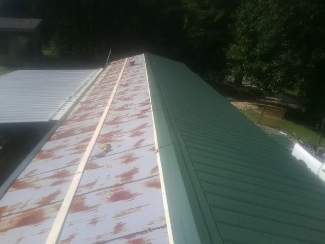 Old rusted panels beside newly installed green metal roofing — Wind Damage Roof Repair by Roofing Brothers in Talisheek