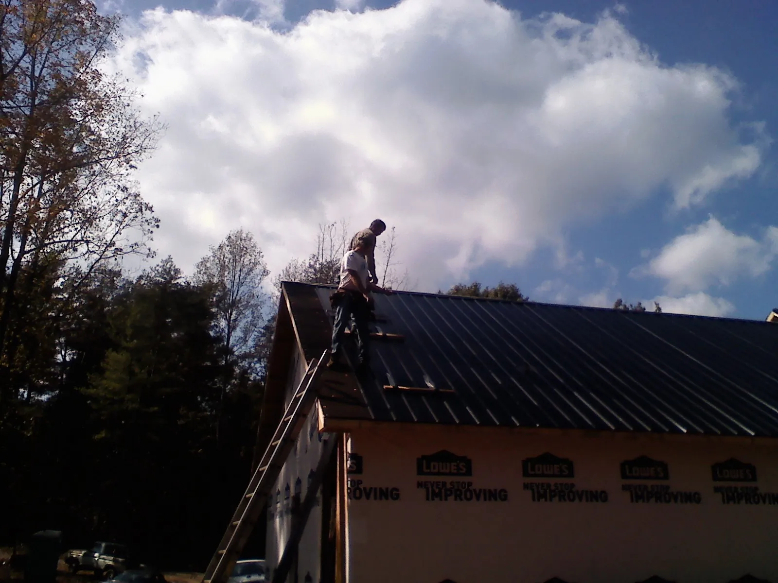 Roofer fastening dark metal panels high against a cloudy sky, from a Roof Inspection job in Talisheek