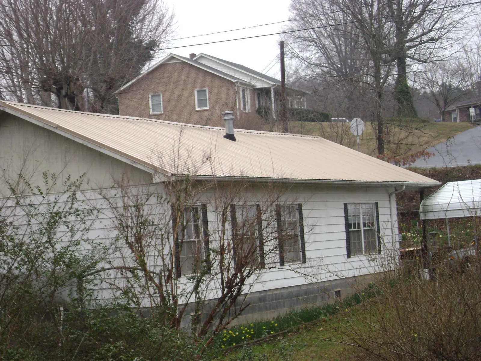Tan metal roof on a white sided house set into a hillside — Commercial Roofing by Roofing Brothers in Talisheek