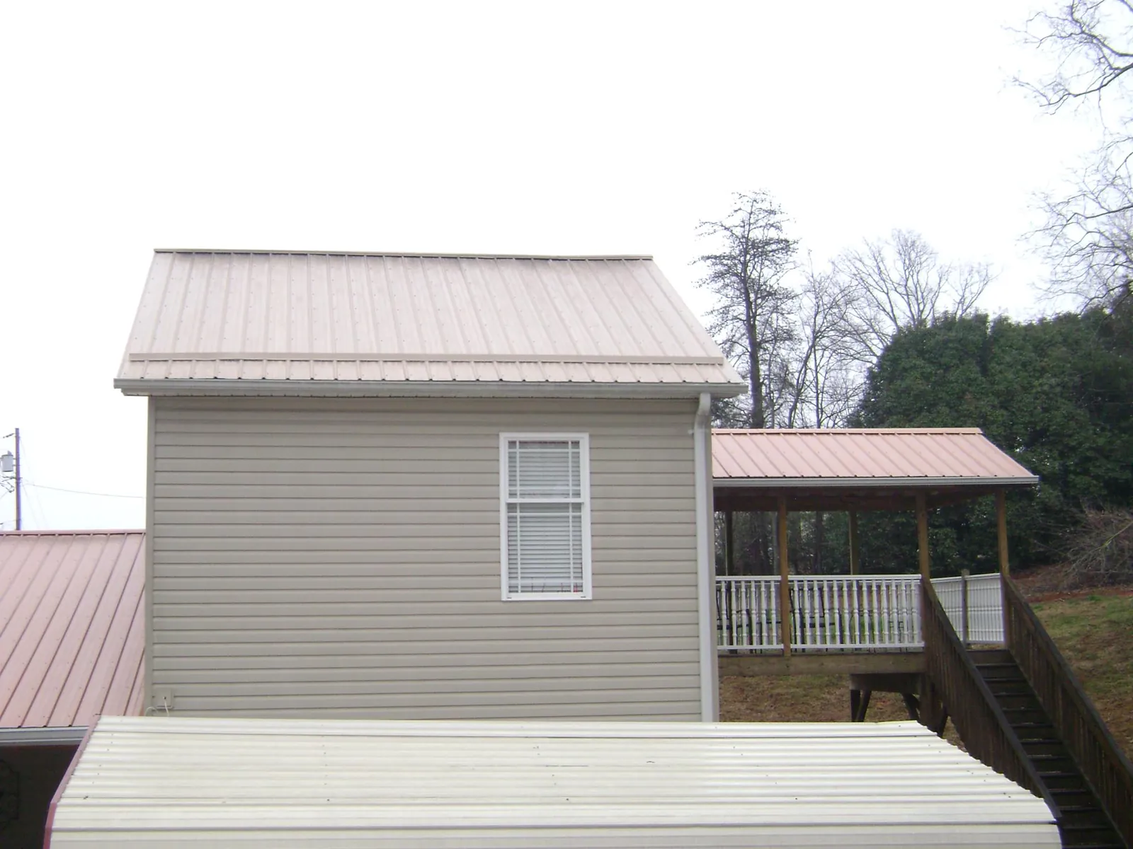 Tan metal roofs on a two story addition and attached porch, from a Roof Replacement job in Talisheek